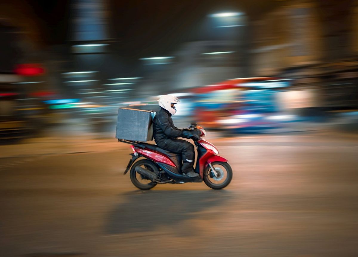 Entregador de moto com baú pela rua à noite